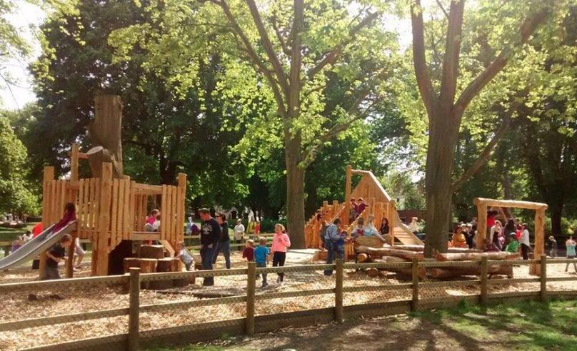 Children playing on wooden play equipment in a leafy Bristol park